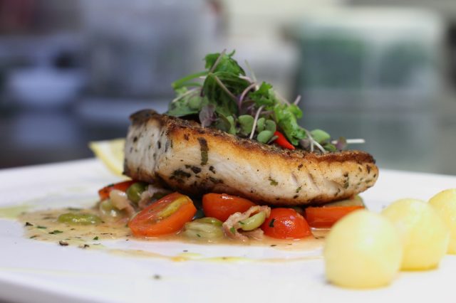 grilled sea bass with sauteed tomatoes served with potatoes ball on white plate