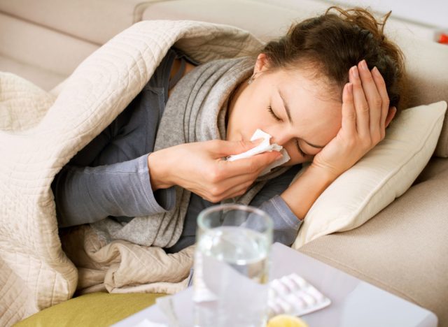 sick women sneezing into tissue while laying down